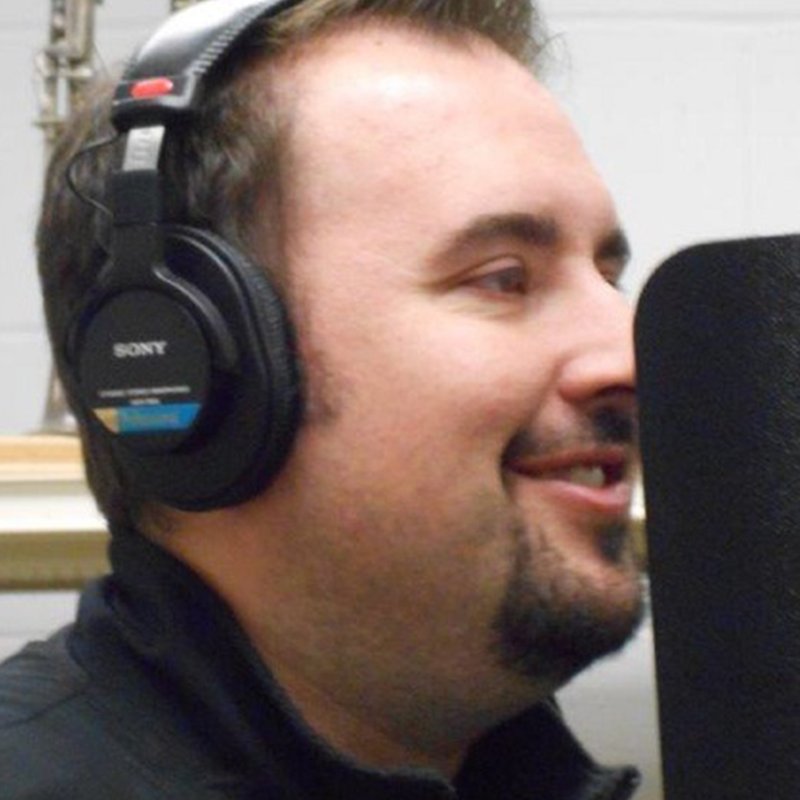 Brandon Guyton in profile, wearing studio headphones and smiling beside a recording microphone.