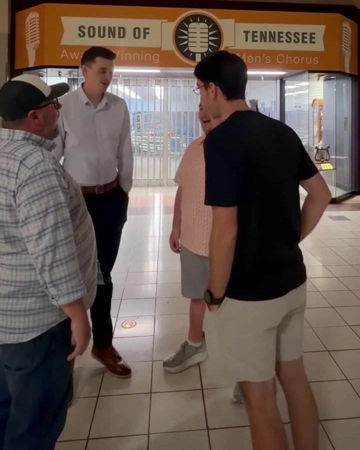 Four men in street clothes standing close together in a mall corridor, under the orange Sound of Tennessee storefront sign.